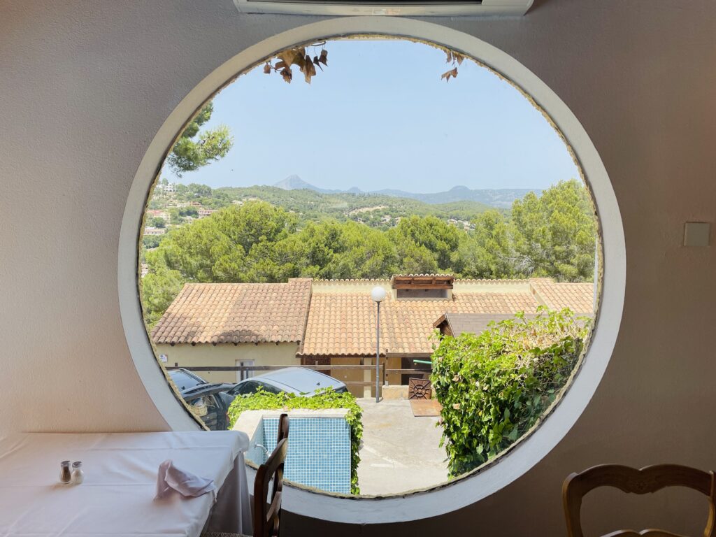 Frühstücksplatz mit Ausblick durch rundes Fenster auf Santa Ponsa und die Berge im Hintergrund