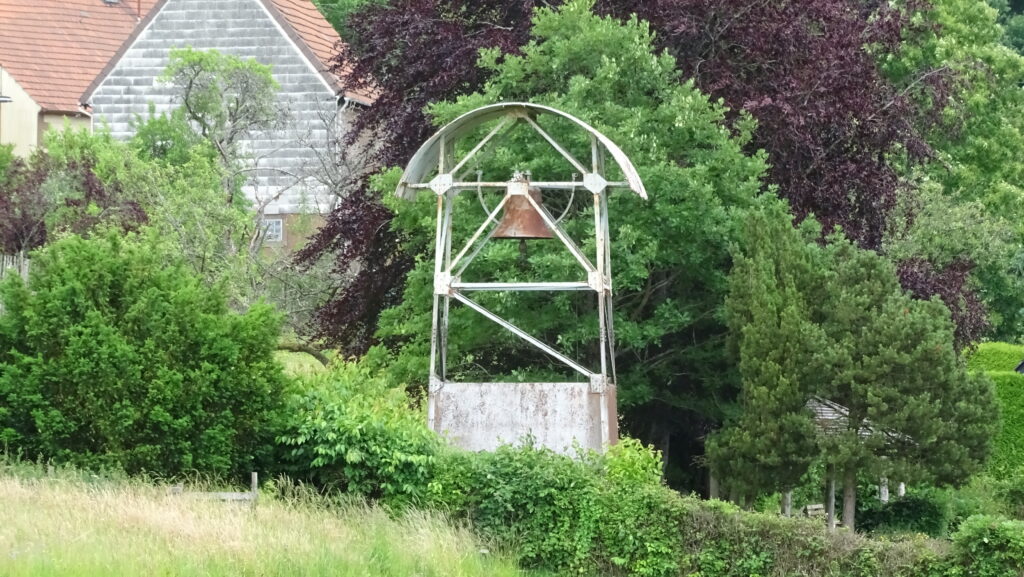 Rostiger Glockenturm aus Metall am Friedhof des Bambergerhofs bei Breitenbach, eingebettet in Bäume