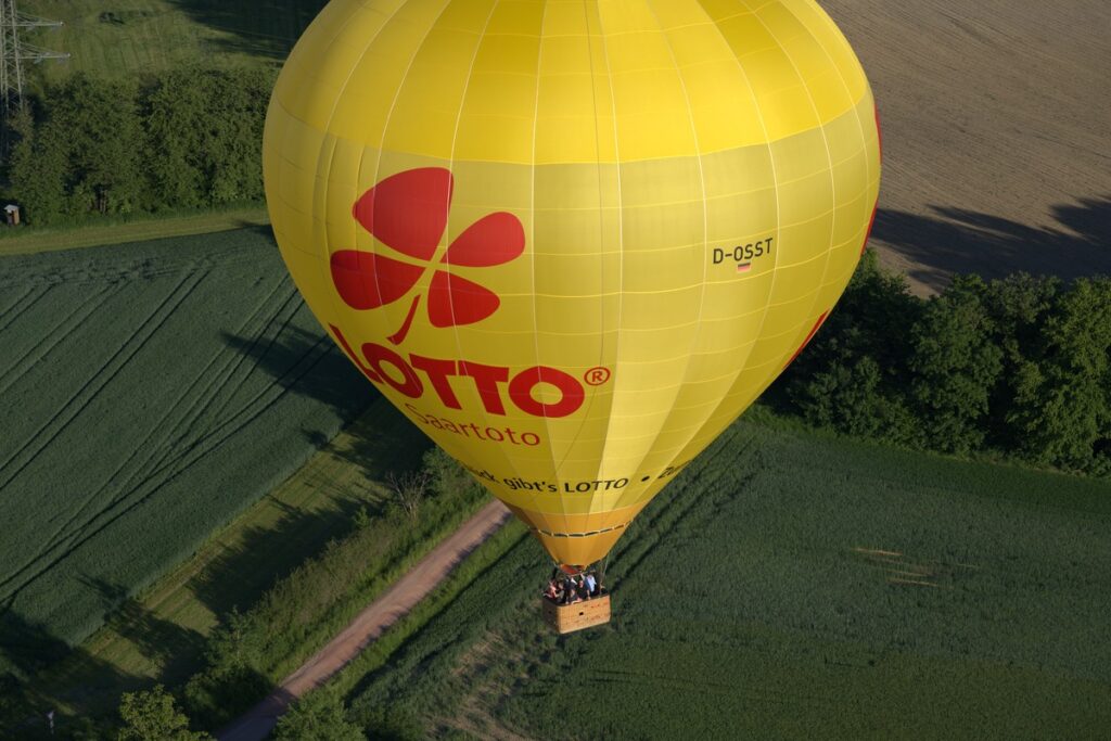Gelber LOTTO-Saartoto-Heißluftballon aus der Luft über Feldern und Wald