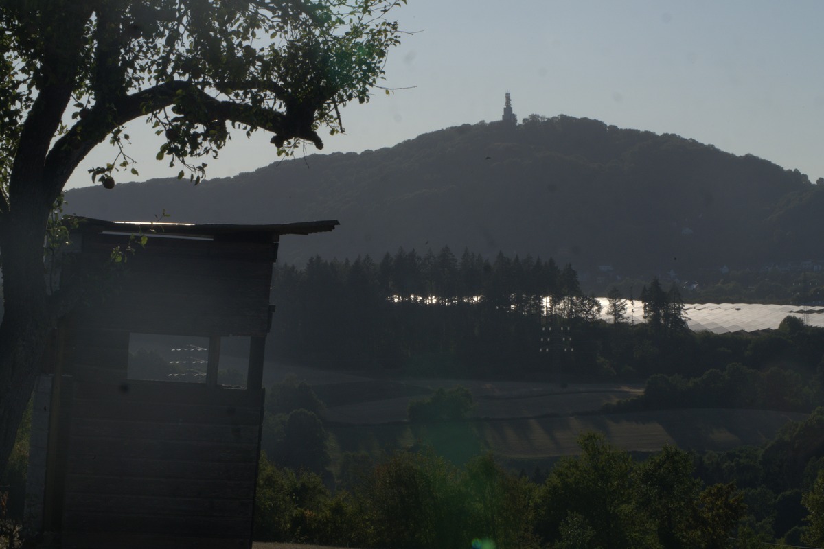 Silhouette eines Hochsitzes und Baum vor Hügelpanorama mit Denkmal und Stausee – Wanderung Sonnenfinsternis