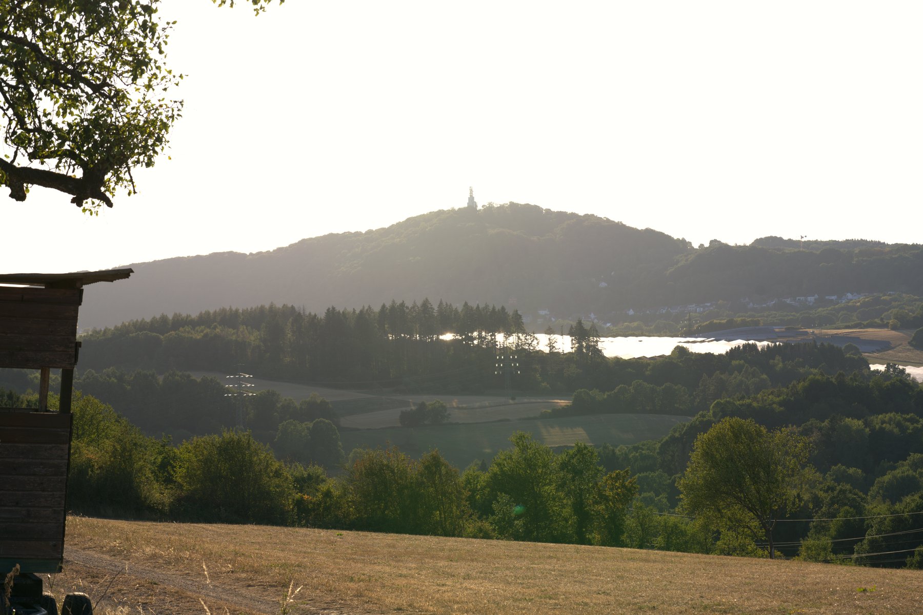 Panoramablick über grüne Hügel mit Denkmal auf dem Gipfel und Stausee im Tal – Wandertour Sonnenfinsternis