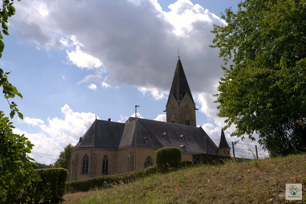 Historische Dorfkirche mit spitzem Turm am Wortsegel-Wanderweg, umgeben von grünen Bäumen